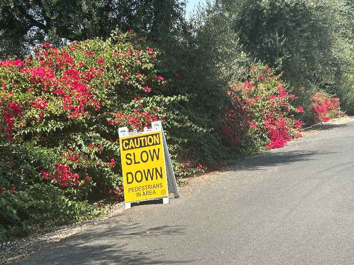 Image of a new project surrounding the Glendora Country Club with a yellow Caution Slow Down sign on the side of the road with bushes outlining the road